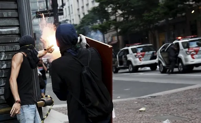 A demonstrator (L) sets off a flare bomb against riot police during a protest against fare hikes for city buses in Sao Paulo, Brazil, January 8, 2016. (Photo by Nacho Doce/Reuters)