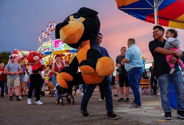 A man smiles as he carries the giant stuffed animal he won at the Iowa State Fair in Des Moines, Iowa on August 13, 2023. (Photo by Evelyn Hockstein/Reuters)