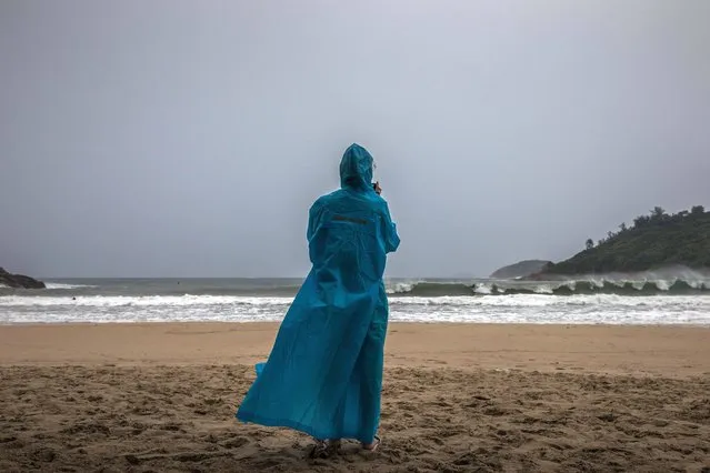 A woman wearing a raincoat watches surfers riding waves generated by Typhoon Saola at a beach in Hong Kong on September 1, 2023. Hong Kong grounded flights, shut down its stock market and closed schools on September 1 as Super Typhoon Saola barrelled towards China's southern coast. (Photo by Dale de la Rey/AFP Photo)