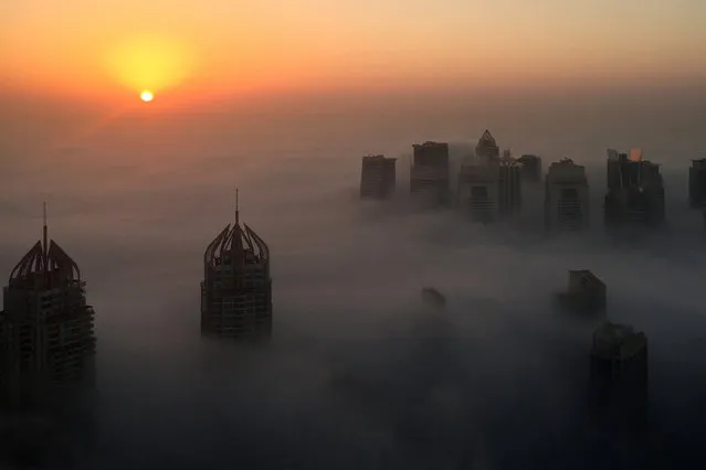 The sun rises behind skyscrapers amidst the clouds on a foggy morning in Dubai on December 5, 2016. (Photo by Rene Slama/AFP Photo)