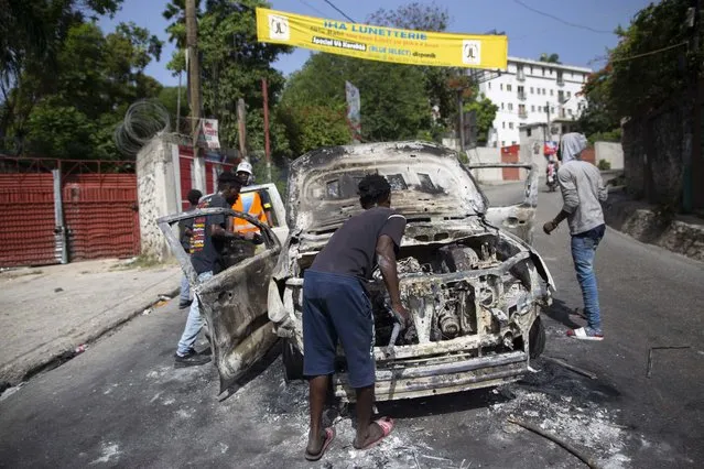 People try to recover usable material from a burned-out car during a protest a day after the murder of President Jovenel Moise, in Port-au-Prince, Haiti, Thursday, July 8, 2021. (Photo by Joseph Odelyn/AP Photo)