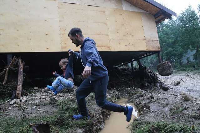 Local residents are seen by a house in the village of Aromat damaged by the overflow of the Kokkozka River in Crimea, Russia on July 4, 2021. According to the local branch of Russia's Federal Service for Hydrometeorology and Environmental Monitoring (Roshydromet), heavy rains are expected in western, southern, eastern, and central regions of Crimea on July 4 and 5. (Photo by Sergei Malgavko/TASS)