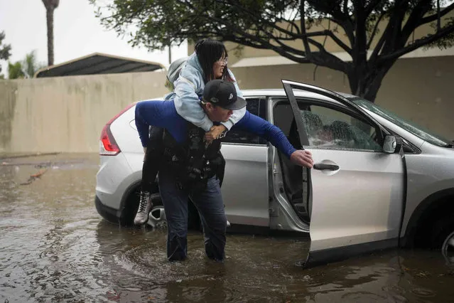 Santa Barbara Police Dept. detective Bryce Ford helps a motorist out of her car on a flooded street during a rainstorm, Thursday, December 21, 2023, in Santa Barbara, Calif. (Photo by Jae C. Hong/AP Photo)