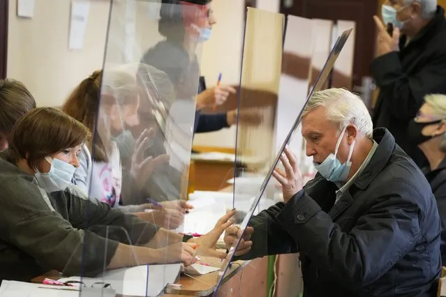 A man is handed his ballots through a safety glass protecting from coronavirus infection during the State Duma, the Lower House of the Russian Parliament and local parliaments elections at a polling station in St. Petersburg, Russia, Friday, September 17, 2021. Russia has begun three days of voting for a new parliament that is unlikely to change the country's political complexion. There's no expectation that United Russia, the party devoted to President Vladimir Putin, will lose its dominance in the State Duma. (Photo by Dmitri Lovetsky/AP Photo)