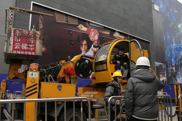 Men work with a crane near an advertisement at a shopping mall in Beijing, Wednesday, January 17, 2024. China's economy for the October-December quarter grew at a quicker rate, allowing the Chinese government to hit its target of about 5% annual growth for 2023 even though trade data and the economic recovery remain uneven. (Photo by Ng Han Guan/AP Photo)