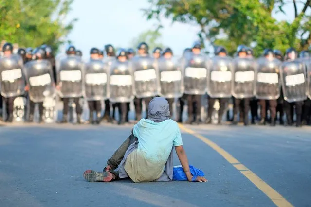 A migrant from Central America sits on a road in front of a Guatemalan police officers after a migrant caravan was blocked by Guatemalan authorities, near the border with Honduras outside of Puerto Barrios, Guatemala, January 16, 2022. (Photo by Josue Decavele/Reuters)
