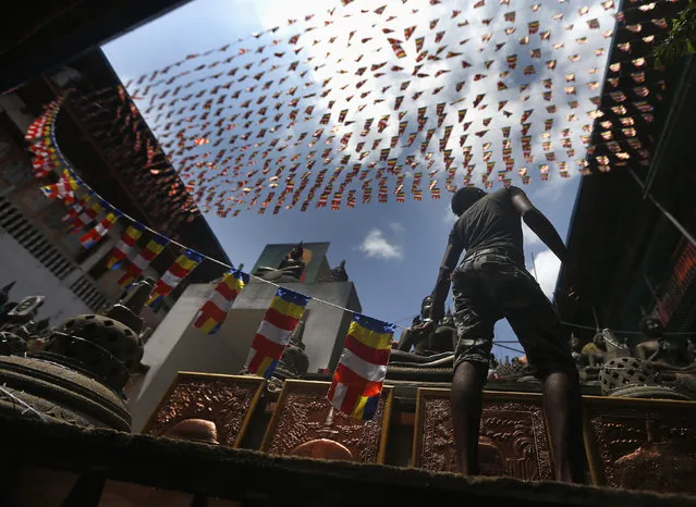 A man holds a line of Buddhist flags while decorating a pandal at a temple ahead of Vesak Day celebrations in Colombo May 13, 2014. Vesak Day, which is celebrated on May 14 and 15 in Sri Lanka, commemorates the birth, enlightenment and death of Buddha. (Photo by Dinuka Liyanawatte/Reuters)