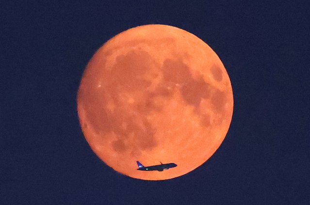 An aircraft passes in front of the moon, with a red glow attributable to smoke particles carried in the upper atmosphere from North American wildfires, a day ahead of the full super moon, as seen from Parliament Hill in London, Britain, on August 18, 2024. (Photo by Toby Melville /Reuters)