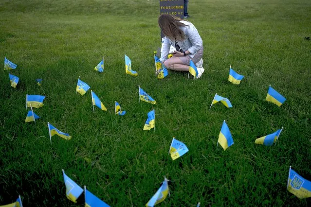 A woman places a flag to honor soldiers killed fighting Russian troops during Kyiv Day celebrations in Kyiv, Ukraine, Sunday, May 29, 2022. (Photo by Natacha Pisarenko/AP Photo)