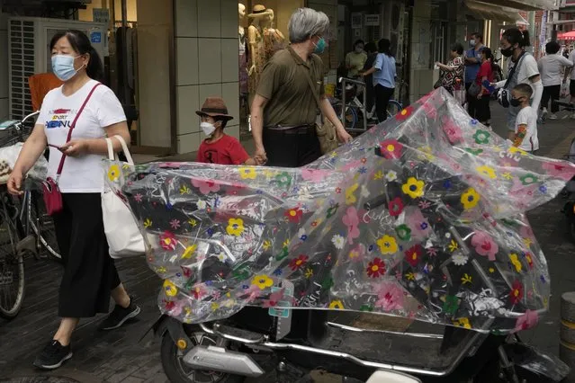 Residents wearing masks past by a bike covered with a flower pattern rain cover, Monday, June 27, 2022, in Beijing. (Photo by Ng Han Guan/AP Photo)