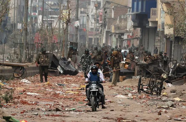 Men ride a motorcycle past security forces patrolling a street in a riot affected area after clashes erupted between people demonstrating for and against a new citizenship law in New Delhi, India, February 26, 2020. (Photo by Adnan Abidi/Reuters)