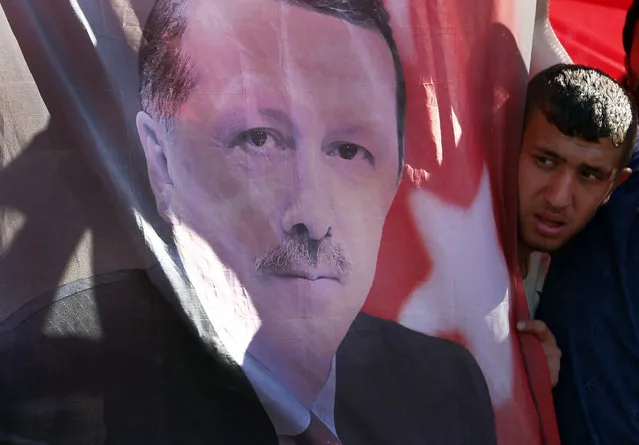 A Turkish man looks towards a portrait of Turkish President Recep Tayyip Erdogan during a protest against the military coup outside Turkey's parliament near the Turkish military headquarters in Ankara, Turkey, Saturday, July 16, 2016. Forces loyal to Turkey's President Recep Tayyip Erdogan quashed a coup attempt in a night of explosions, air battles and gunfire that left dozens dead Saturday. (Photo by Hussein Malla/AP Photo)
