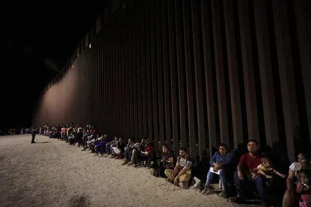 Migrants wait along a border wall Tuesday, August 23, 2022, after crossing from Mexico near Yuma, Ariz. (Photo by Gregory Bull/AP Photo)