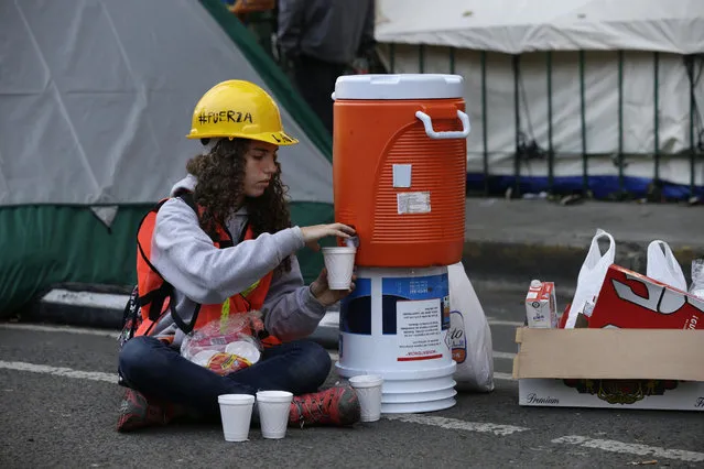 A volunteer fills cups with coffee on the periphery of search and rescue site of a felled office building brought down by a 7.1-magnitude earthquake, in the Roma Norte neighborhood of Mexico City, Sunday, September 24, 2017. As rescue operations stretched into day 6, residents throughout the capital have held out hope that dozens still missing might be found alive. (Photo by Marco Ugarte/AP Photo)