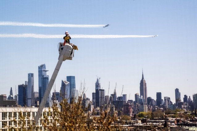 A PSE&G utility worker watches the Navy's Blue Angels and the Air Force's Thunderbirds conduct “a collaborative salute” to honor those battling the COVID-19 pandemic with a flyover of New York and New Jersey, Tuesday, April 28, 2020, in this view from Jersey City, N.J. (Photo by Charles Sykes/Invision/AP Photo)
