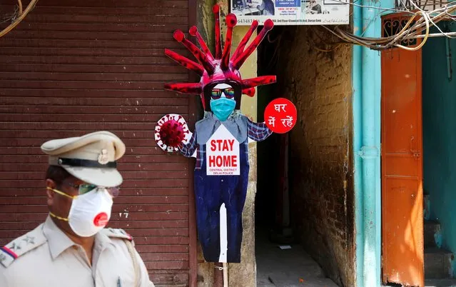A police officer wearing a protective face mask walks past a novel coronavirus-themed scarecrow cutout put up in a residential area during an extended lockdown to slow the spreading ofthe coronavirus disease (COVID-19) in the old quarters of Delhi, India, April 30, 2020. (Photo by Adnan Abidi/Reuters)