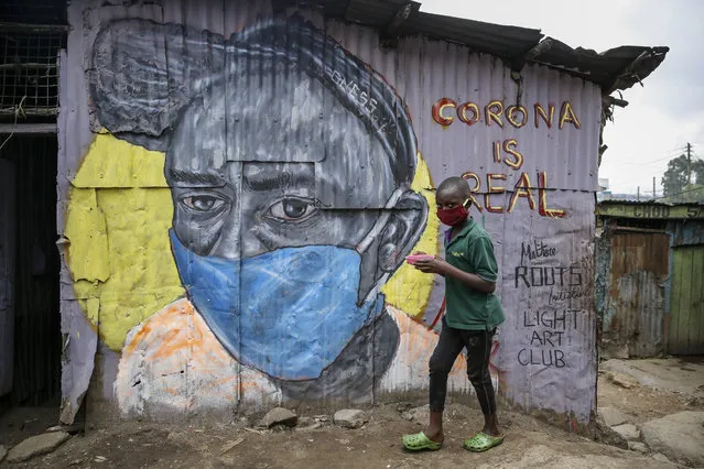 A boy wearing a face mask carries a small bowl of “githeri”, or mixed beans and maize, for him to eat as he walks past an informational mural warning people about the risk of the new coronavirus, painted by graffiti artists from the Mathare Roots youth group, in the Mathare slum, or informal settlement, of Nairobi, Kenya Saturday, April 18, 2020. Africa now has more than 1,000 deaths from COVID-19, the Africa Centers for Disease Control and Prevention said Saturday, with 52 of the continent's 54 countries having reported cases. (Photo by Brian Inganga/AP Photo)