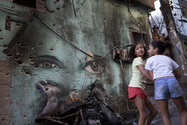 In this September 27, 2017 file photo, girls walk past a wall riddled with bullet holes from shootings between rival drug traffickers, at the Rocinha slum, in Rio de Janeiro, Brazil. Violence is on the rise in Rio's slums after several years of decline, and the killings of kids have shocked even residents long inured to deaths from gangs and police. (Photo by Silvia Izquierdo/AP Photo)