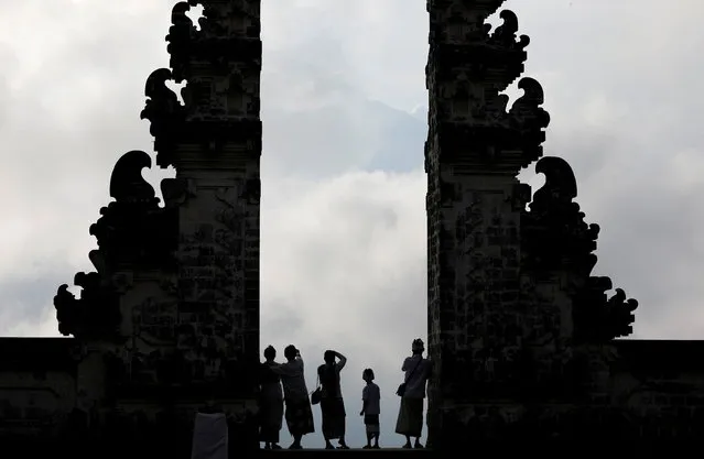 Balinese worshippers look at Mount Agung, enshrouded by clouds, from the gate of Penataran Agung Lempuyang temple, a day after the volcano's alert status was raised to the highest level, in Karangasem Regency, on the resort island of Bali, Indonesia September 23, 2017. (Photo by Darren Whiteside/Reuters)