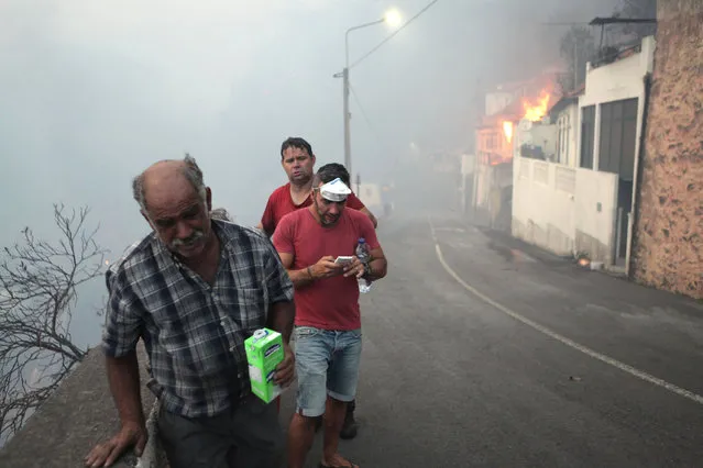 People are seen on the streets of Bom Sucesso, near to a fire during the wildfires at Funchal, Madeira island, Portugal, August 9, 2016. (Photo by Duarte Sa/Reuters)