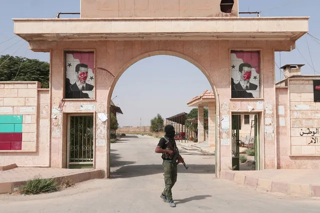 A Kurdish fighter from the People's Protection Units (YPG) carries his weapons as he stands outside the faculty of agricultural engineering, where defaced pictures of Syrian President Bashar al-Assad are seen at the entrance's gate, in the northeastern city of Hasaka, Syria, August 21, 2016. (Photo by Rodi Said/Reuters)