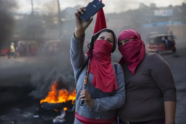 Masked supporters of presidential candidate Salvador Nasralla take a selfie at a burning roadblock set up by demonstrators protesting what they call electoral fraud in Tegucigalpa, Honduras, Friday, December 1, 2017. (Photo by Rodrigo Abd/AP Photo)