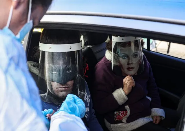 A healthcare worker conducts a rapid COVID-19 test on Ignacio Poblete, wearing a face shield face with an image of Batman, accompanied by his mother Marisol Aro, using a face shield with an image of Wonder Woman, in Santiago, Chile, Saturday, June 27, 2020. Poblete's father bought the face shields who has since been infected with the new coronavirus and is now intubated in an intensive care unit. (Photo by Esteban Felix/AP Photo)