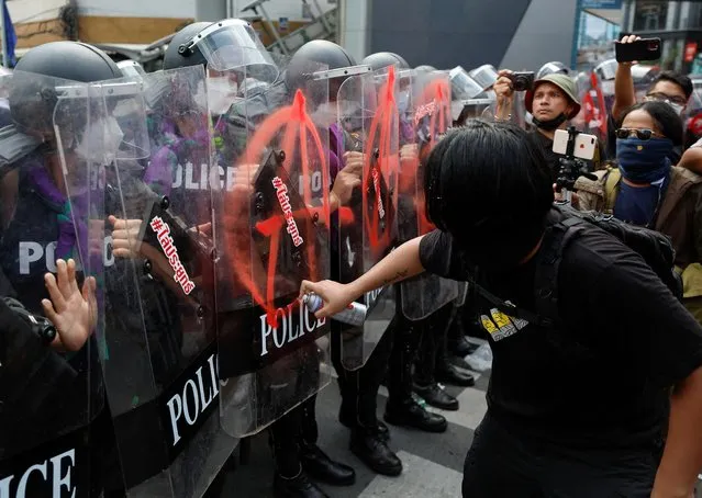 A demonstrator spray paints shields help up by police officers during a protest against the Asia-Pacific Economic Cooperation (APEC) Summit near the Queen Sirikit National Convention Center venue, at Asoke Junction, in Bangkok, Thailand on November 17, 2022. (Photo by Jorge Silva/Reuters)