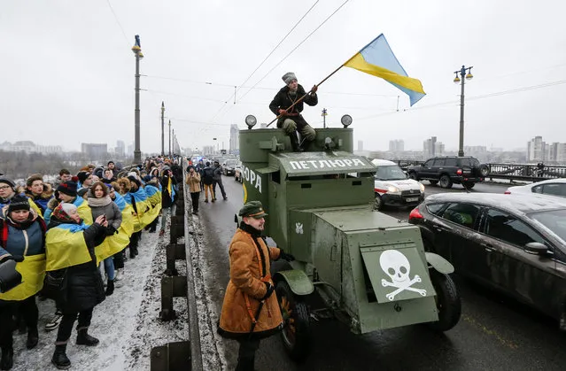 Ukrainians carry a National flag as they form a symbolic chain across a bridge, linking the left and right banks of Dnieper River in Kiev, Ukraine, 22 January 2018. The Ukraine is celebrating the anniversary of unification of East and West Ukraine in 1919. A historical armored car drive on a road along of people. (Photo by Sergey Dolzhenko/EPA/EFE)