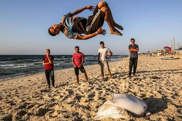 A youth performs a flip as others watch along a beach by the Mediterranean Sea shore in Rafah in the southern Gaza Strip at sunset on September 2, 2020. (Photo by Said Khatib/AFP Photo)