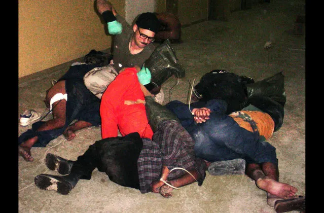 In this undated photo, Charles Graner, a U.S. Army reservist appears poised to punch a Iraqi detainee at Abu Ghraib Prison as other detainees lay bound at the hands and hooded. Detainee at right appears to be partially clothed. Outrage among Iraqis and much of the world erupted as photographic evidence surfaced of torture and abuse inside the prison in 2004. (Photo courtesy of Washington Post/The Atlantic)