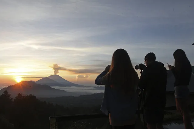 Tourists take photos of the Mount Agung volcano during a sunrise in Kintamani, Bali, Indonesia, Wednesday, December 13, 2017. Indonesia's disaster mitigation agency said the volcano remains at its highest alert level but most of Bali is safe for tourists. (Photo by Firdia Lisnawati/AP Photo)