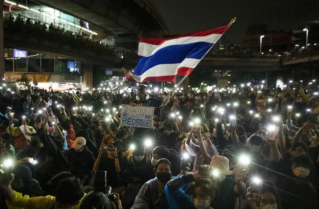 Pro-democracy protesters wave the Thailand national flag as others shine their mobile phone lights during an anti-government protest in Bangkok, Thailand, Sunday, October 18, 2020. Thai police on Sunday declined to say whether they were taking a softer approach toward student anti-government demonstrations, after several mass rallies attracting thousands of protesters ended peacefully in Bangkok on Saturday. (Photo by Sakchai Lalit/AP Photo)