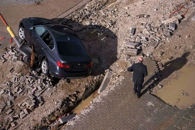 A pedestrian walks by cars on a damaged street after heavy rain in Kosovo, in Skenderaj on January 20, 2023. (Photo by Armend Nimani/AFP Photo)