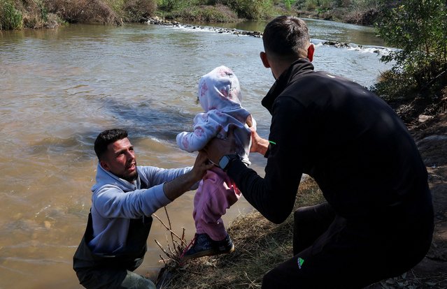 A Syrian who fled the violence in western Syria, carries a child near the Nahr El Kabir River, after the reported mass killings of Alawite minority members, in Akkar, Lebanon on March 11, 2025. (Photo by Mohamed Azakir/Reuters)