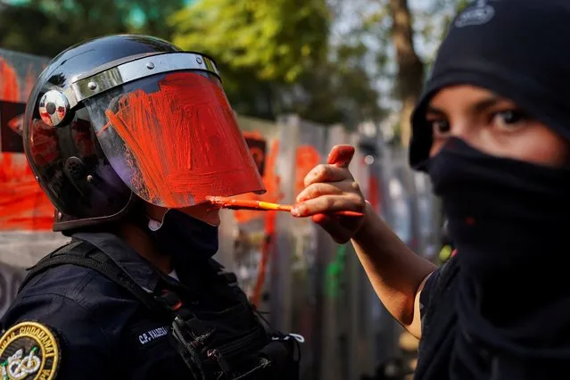 A member of a feminist collective paints the helmet of a riot police officer during a protest against gender and police violence, in Mexico City, Mexico on November 11, 2020. (Photo by Toya Sarno Jordan/Reuters)