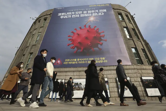 People wearing face masks as a precaution against the coronavirus walk under a banner emphasizing an enhanced social distancing campaign in front of Seoul City Hall in Seoul, South Korea, Wednesday, November 25, 2020. The banner reads: “We have to stop before COVID-19 stops everything”. (Photo by Ahn Young-joon/AP Photo)