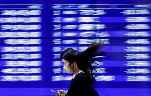 A passerby walks past an electric monitor displaying recent movements of various stock prices outside a bank in Tokyo, Japan on March 22, 2023. (Photo by Issei Kato/Reuters)