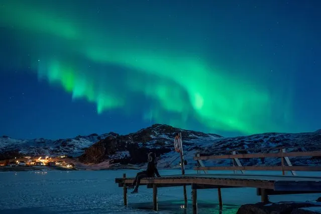 A woman sits on a pier on March 3, 2018 to watch northern lights (Aurora borealis), on the Lofoten Islands, in Bostad, in the arctic circle in northern Norway. (Photo by Olivier Morin/AFP Photo)