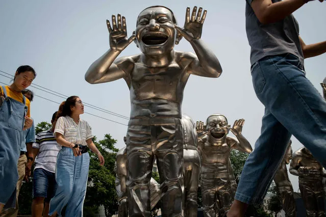 People walk passed sculptures by Chinese artist Minjun Yue on a street outside a museum in Beijing, China on July 5, 2018. (Photo by Nicolas Asfouri/AFP Photo)