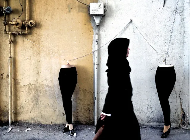 An Iranian woman walks past mannequins locked to a gas pipe in northern Tehran on December 15, 2014. (Photo by Behrouz Mehri/AFP Photo)