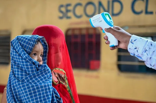 A health worker checks the body temperature of a passenger during a Covid-19 coronavirus screening as she arrives with her child at a railway platform on a long distance train, in Mumbai on June 8, 2021. (Photo by Punit Paranjpe/AFP Photo)