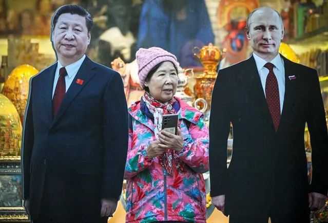 A tourist stands next to cardboard images depicting Chinese President Xi Jinping (L) and his Russian counterpart Vladimir Putin at the touristic Arbat street in downtown Moscow on November 15, 2023. (Photo by Alexander Nemenov/AFP Photo)