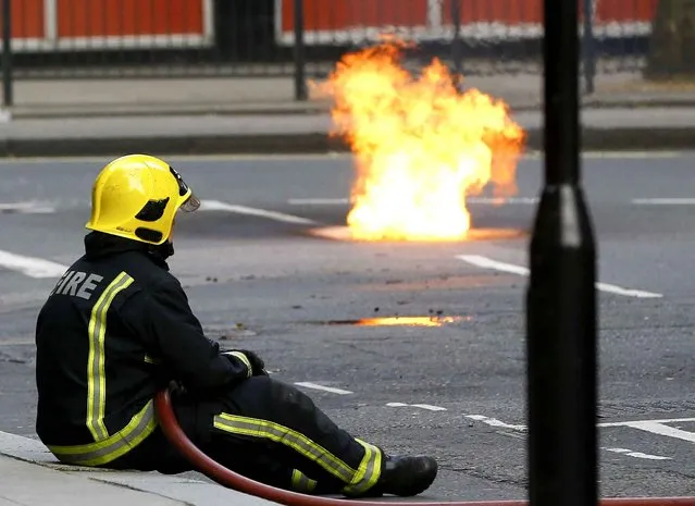 A fireman watches as flames come out of a manhole cover in the road, an electrical fire under the pavement near Holborn in London, Wednesday, April 1, 2015. People have been evacuated from nearby buildings. (Photo by Kirsty Wigglesworth/AP Photo)