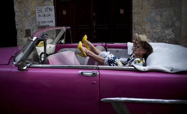 A tourist kicks up her heels as she and a friend wait for the driver of a hot pink private taxi, a classic American Chevrolet convertible, before they take a driving tour of Havana, Cuba, Wednesday, January 31, 2018. (Photo by Ramon Espinosa/AP Photo)