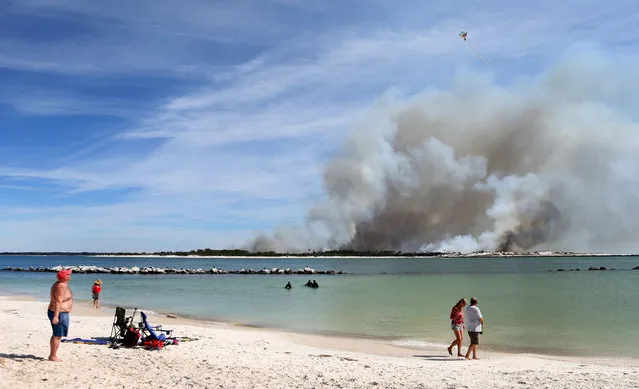 Beach goers enjoy at St. Andrews State Park in Panama City Beach, Fla. as a controlled fire releases smoke over Shell Island on Wednesday, March 2, 2016. (Photo by Patti Blake/News Herald via AP Photo)