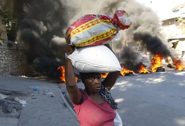 A woman walks past burning tires set on fire by protesters to call attention to the country's insecurity and demanding the resignation of the prime minister, in Port-au-Prince, Haiti, Thursday, January 18, 2024. (Photo by Odelyn Joseph/AP Photo)