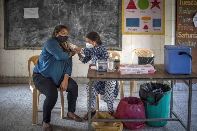 A health worker inoculates a woman during a vaccination drive against coronavirus inside a school in New Delhi, India, Wednesday, October 20, 2021. India is nearing a milestone of administering a total of one billion doses against COVID-19. (Photo by Altaf Qadri/AP Photo)