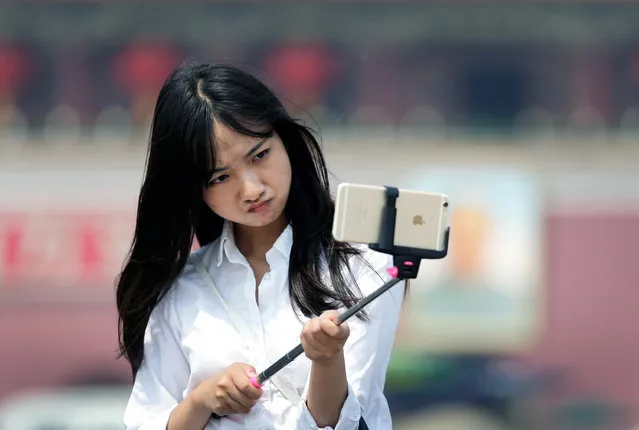 A woman reacts as she uses a selfie stick to take a photo of herself at Tiananmen Square in Beijing, China, Thursday, April 30, 2015. Selfie sticks are gaining popular in China, and many people are using them at popular tourist destinations. (Photo by Andy Wong/AP Photo)