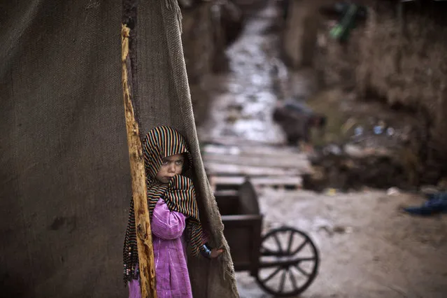 An Afghan refugee girl, looks at men trying to clear sewage paths so rainwater can drain, in an attempt to avoid flooding during a heavy rainfall, in a poor neighborhood on the outskirts of Islamabad, Pakistan, Tuesday, March 11, 2014. For more than three decades, Pakistan has been home to one of the world’s largest refugee communities: hundreds of thousands of Afghans who have fled the repeated wars and fighting their country has undergone. (Photo by Muhammed Muheisen/AP Photo)